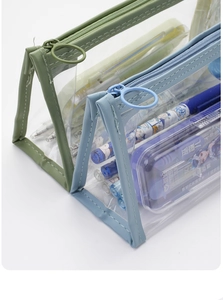 Detail view of transparent PVC pencil cases with green and blue leather trim and ring zippers