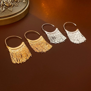 Macro detail of elegant C-shaped metal tassel earrings in gold and silver finishes