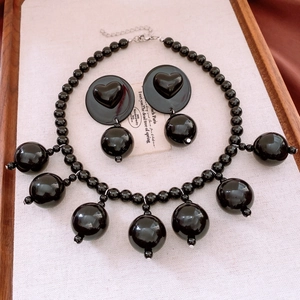 Detail view of a black acrylic jewelry set with bead necklace and heart earrings on wood