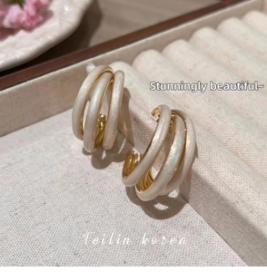 Macro detail of triple-layered C-shaped gold-plated earrings with cream enamel finish