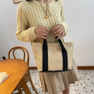 Detail of beige straw tote bag with black handles held by model in natural light