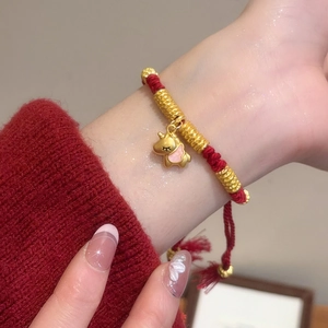 Detail of red braided silk bracelet featuring a gold unicorn charm with pink enamel accents