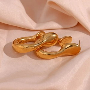 Macro shot of gold irregular fluid-shaped hoop earrings on soft pink silk fabric