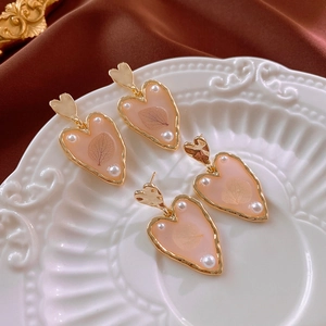 Detail of heart earrings with gold plating, pink resin, leaf texture and white pearls