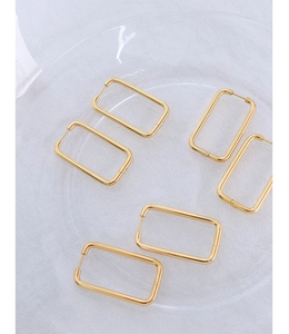 Detailed view of six gold rectangular hoop earrings set on a glass tray for women