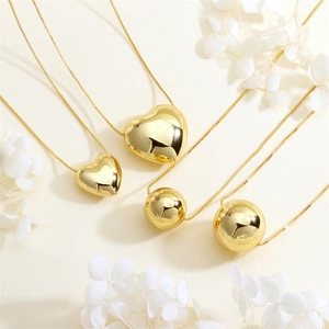 Polished gold heart and ball necklaces with fine box chains on elegant background