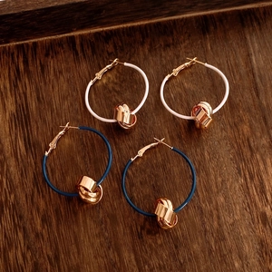 Close-up of white and dark blue twisted circular pendant earrings with 18K gold knot detail