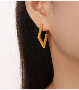 Close-up of golden geometric rhombus earrings on model featuring a sleek metallic texture