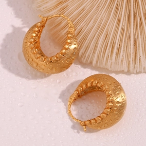 Macro detail of 18K gold plated hoop earrings with textured surface and water droplets