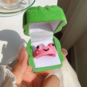 Pink resin frog ring held next to a green velvet frog shaped jewelry gift box