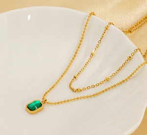 Close-up of a double-layered gold necklace with an emerald zircon pendant in a shell dish