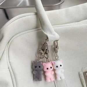 Detailed view of three flocked cat charms in grey, pink and white on a canvas bag