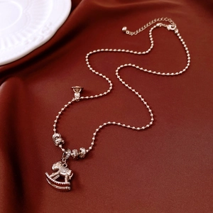 Détail du pendentif cheval à bascule en or rose avec zircons sur fond de soie rouge