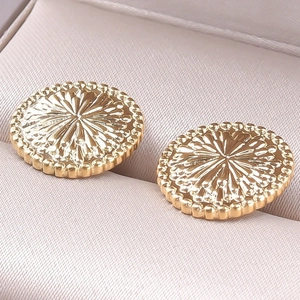 Close-up of golden stainless steel stud earrings with sunburst texture in a silk gift box