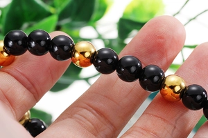 Close-up of black and gold beaded elastic bracelet featuring cross religious theme