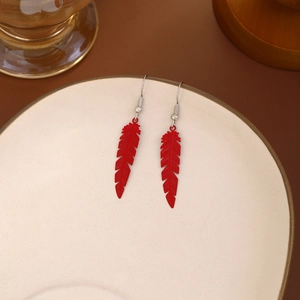 Detail shot of bright red feather-shaped earrings hanging on a ceramic plate edge