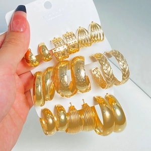 Close-up of a hand holding textured gold C-shaped earrings with woven and wavy patterns