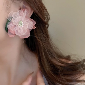 Pink fabric flower earring with beaded center shown on model in soft lighting