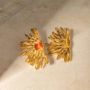 Detail of 18k gold-plated sunburst earrings with red cat's eye stone on stone surface