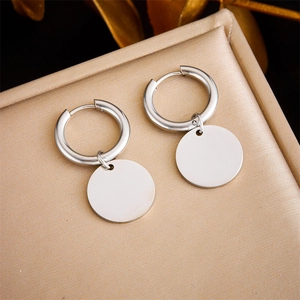 Close-up of silver hoop earrings with polished disc pendants on golden textured pad