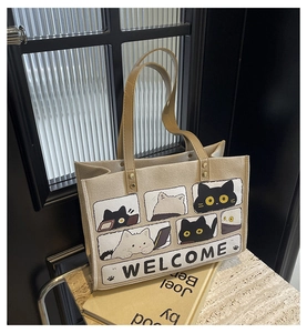 Detail of beige canvas tote bag with black and white cat prints and brown PU handles