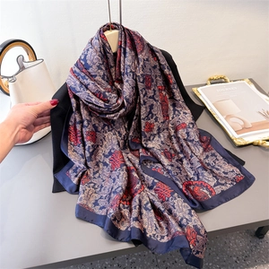 Écharpe en soie bleu marine avec motifs rouges et imprimé paisley doré sur un magazine
