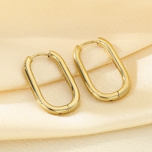 Close-up of golden oval hoop earrings on beige silk fabric with smooth metal finish