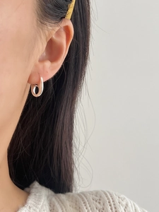 Close-up of minimalist silver oval hoop earrings worn by a model in casual knitwear