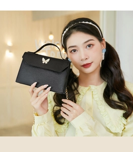Detail of a mini black crossbody bag with white butterfly clasp and golden chain