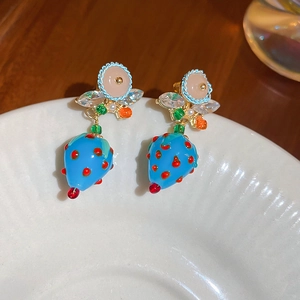 Detail of blue strawberry earrings with crystal accents on a white ceramic plate