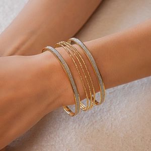 Detail of layered gold bangles set with frosted sequins and textured metallic finish