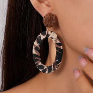 Close-up of model wearing leopard print fabric oval hoop earrings with brown woven studs