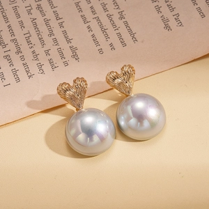 Detailed view of heart-shaped gold studs with large iridescent pearls on a beige surface