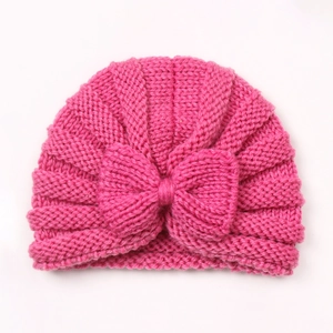 Detail of rose pink baby knitted hat featuring a large textured bow on a flat surface