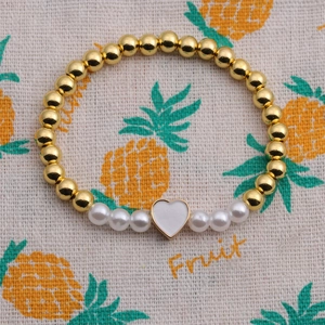 Detail of gold beaded pearl bracelet with a white heart charm on a textured background