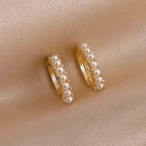 Minimalist gold hoop earrings with small white pearls on champagne silk background