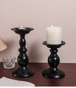 Detail of matte black metal candle holders on a wooden table with soft lighting