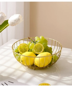 Close-up of a luxury gold wire fruit basket on a white marble surface with soft shadows