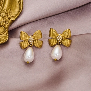Golden butterfly bow earrings with white beads and drop pearl on silk background