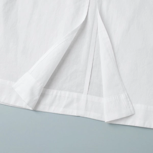 Detailed close-up of white cotton dress hem featuring fine stitching and side slit detail