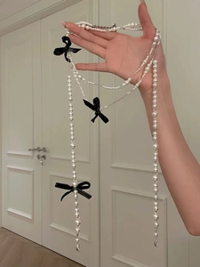 Detail of long pearl necklace with black bows held by hand showing length and drape
