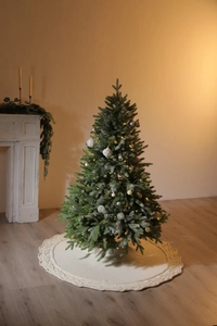 Detail of white knit Christmas tree skirt with festive ornaments and warm lighting
