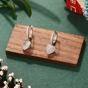 Detail of silver heart-shaped crystal earrings on wooden stand with mesh metal design
