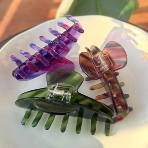 Close-up of three acetate hair claws in purple, green and marble patterns on a white plate