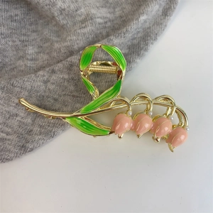 Close-up of golden tulip hair claw with pink enamel buds and green leaves detail