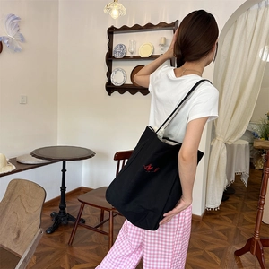 Detail of black canvas tote bag showing striped strap and red embroidered pattern