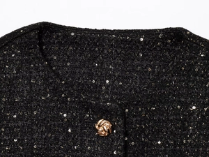 Detail of black tweed vest with gold sequins and textured metal swirl button closure