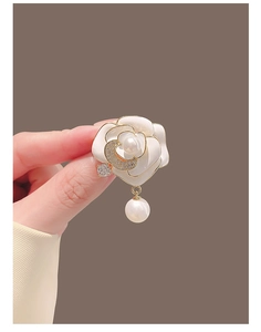 Gros plan détaillé de la broche camélia avec bords dorés, perles et pendentif zircon lune
