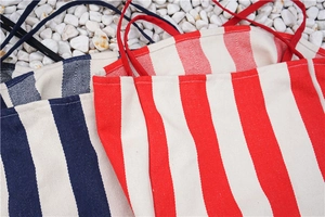 Close-up of thick canvas tote bags with red and navy stripes on white pebbles