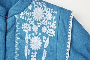 Detailansicht der weißen Blumenstickerei und Wellennaht auf der blauen Denim Baumwolljacke